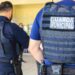 Dois agentes da Guarda Municipal com coletes táticos em ambiente interno