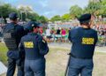 Três agentes da Guarda Civil Municipal observando multidão em evento ao ar livre em parque com lago