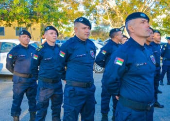 Grupo de guardas municipais em uniforme azul escuro alinhados em formação ao ar livre durante dia ensolarado.