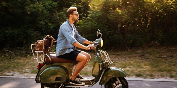 Homem conduzindo ciclomotor verde em via pública, exemplo de veículo que exige registro e habilitação conforme normas de trânsito.