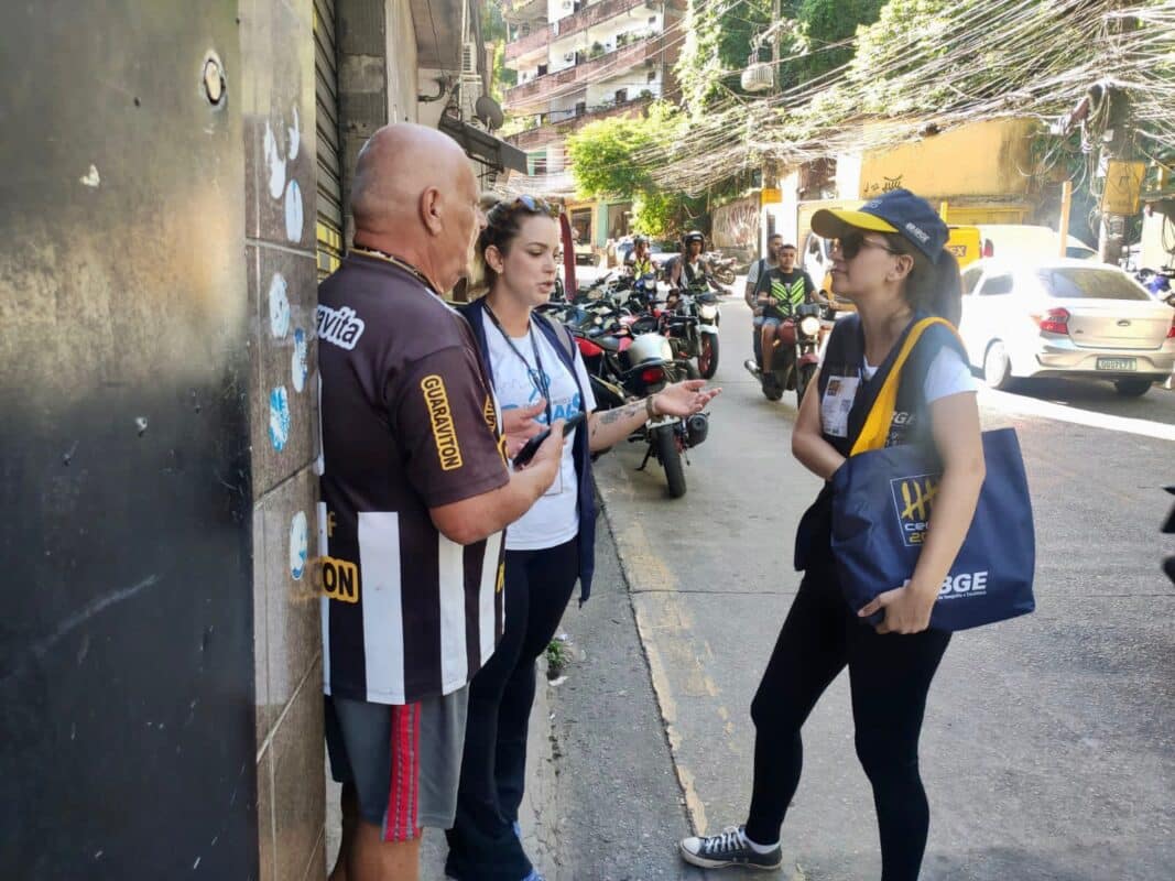 Pesquisadores do IBGE conversando com morador em rua movimentada de área urbana com motocicletas ao fundo