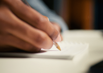 Pessoa escrevendo em um caderno branco com caneta esferográfica dourada em foco
