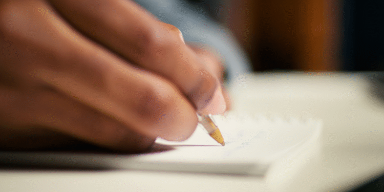 Pessoa escrevendo em um caderno branco com caneta esferográfica dourada em foco