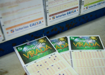 Bilhetes da Mega da Virada sobre superfície próxima a caixa com bilhetes da Loteria Caixa.