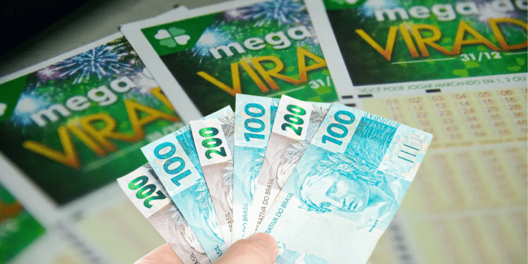 Mão segurando cédulas de real na frente de bilhetes da Mega Virada com fogos de artifício ao fundo.