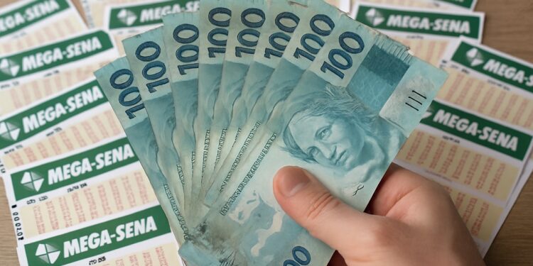 Pessoa segurando notas de cem reais com bilhetes da Mega-Sena ao fundo