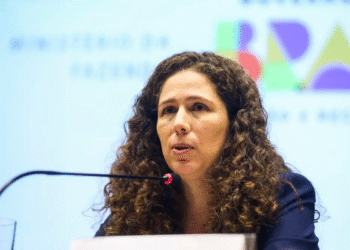 Mulher de cabelos cacheados falando em púlpito com microfone durante evento formal