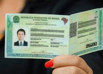 Mão feminina segurando carteira de identidade brasileira aberta com dados pessoais censurados