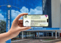 Mão segurando smartphone com carteira de identidade digital na frente do prédio da Previdência Social