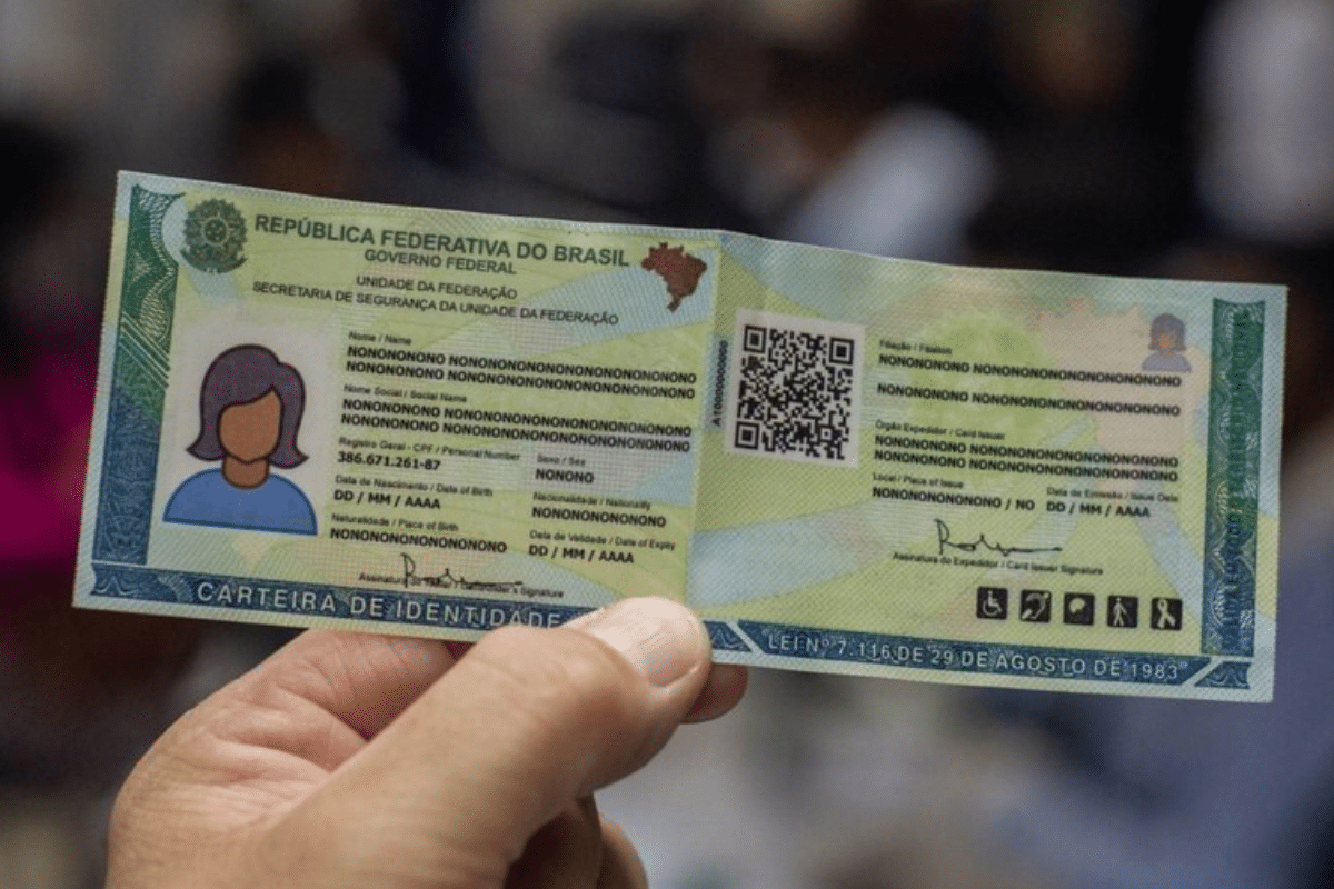 Foto de uma carteira de identidade brasileira com dados fictícios e QR code, sendo segurada por uma mão.