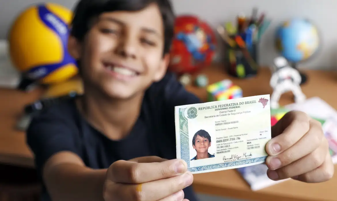 Menino sorrindo segurando carteira de identidade brasileira com detalhes no fundo desfocado