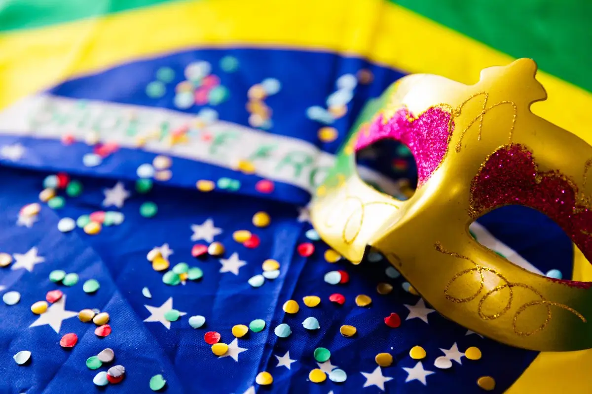 Celebração do Carnaval de 2026: tradição e folga prolongada. Máscara de carnaval sobre a bandeira do Brasil com confetes coloridos.