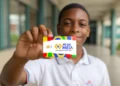 Estudante segurando cartão do programa Pé-de-Meia em frente à escola representando os pagamentos liberados pelo MEC.