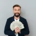 Homem sorrindo segurando notas de dólar, simbolizando grandes ganhos financeiros em profissões bem remuneradas.