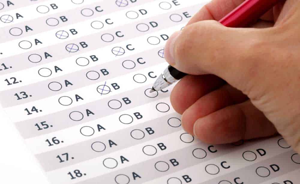 Mão segurando caneta e marcando alternativa em prova de múltipla escolha