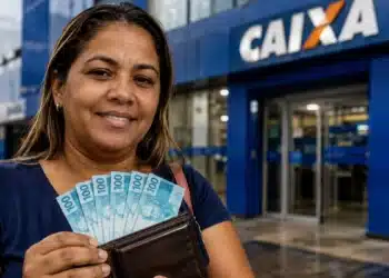 Mulher sorridente segurando carteira com notas de R$ 100 em frente a uma agência da Caixa, representando o Saque Calamidade do FGTS.