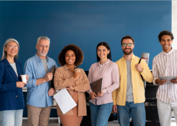 Grupo multicultural de seis profissionais sorrindo em escritório moderno com parede azul