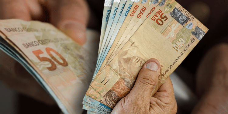 Imagem de notas de 50 reais brasileiras sendo contadas à mão, representando a nova atualização do salário mínimo.