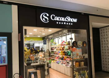 Fachada da loja Cacau Show em shopping, com vidros transparentes mostrando chocolates e produtos na exposição
