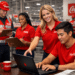Colaboradores da Coca-Cola usando uniformes vermelhos em ambiente industrial com pranchetas e laptop