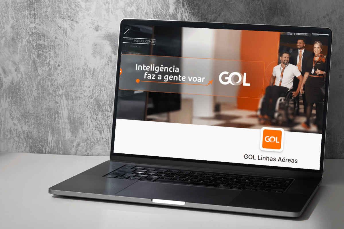 Notebook exibindo site da GOL Linhas Aéreas com slogan "Inteligência faz a gente voar" e equipe da empresa ao fundo