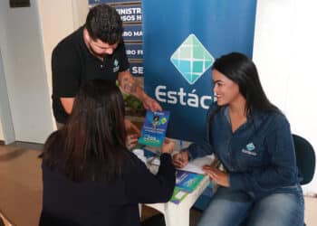 Funcionários da Estácio atendendo aluna e mostrando oferta de preços fixos em folder azul