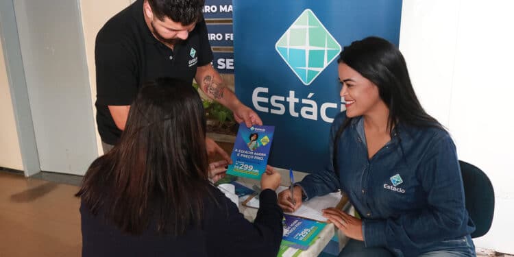 Funcionários da Estácio atendendo aluna e mostrando oferta de preços fixos em folder azul