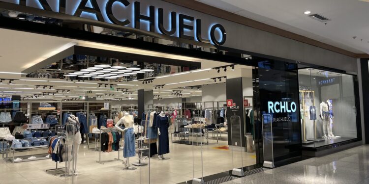 Entrada da loja Riachuelo em shopping com manequins exibindo roupas e iluminação interna