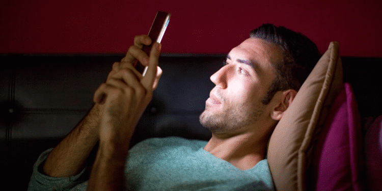 Homem deitado no sofá olhando para a tela do smartphone iluminado à noite