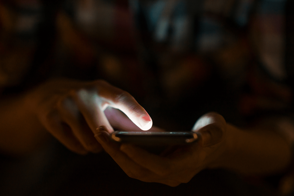 Pessoa tocando na tela de um smartphone com luz brilhando no dedo em ambiente escuro