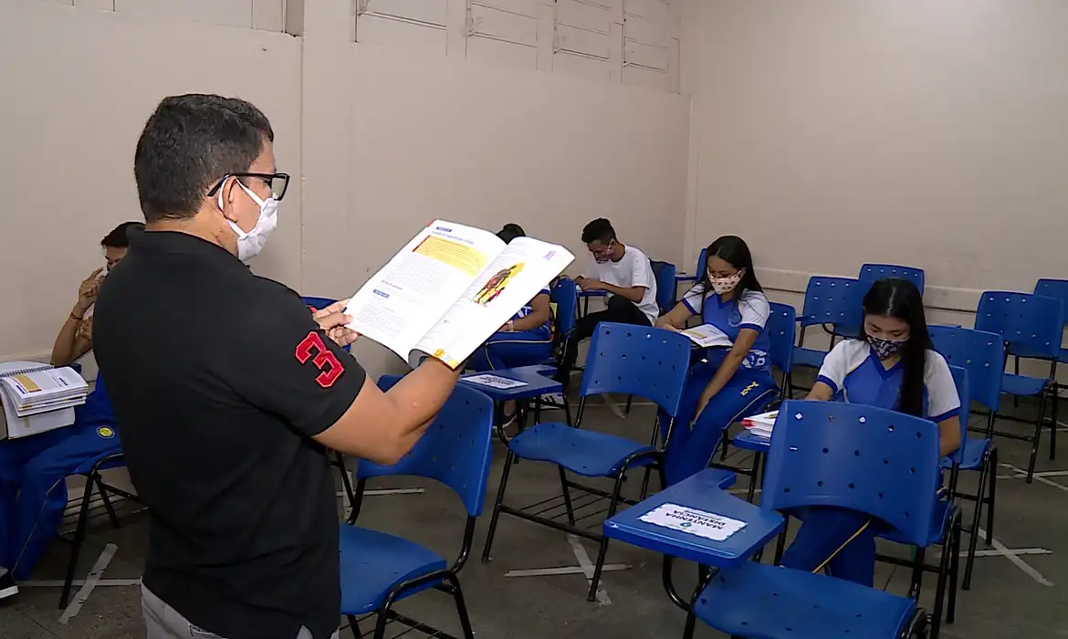 Aula presencial com medidas de prevenção em 2026 Professor dando aula para alunos usando máscaras em sala espaçada, seguindo protocolos