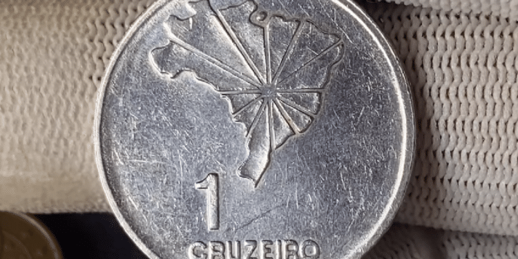 Close de uma moeda antiga de 1 Cruzeiro sendo segurada com cuidado por dedos usando luvas brancas, indicando seu potencial valor como item de colecionador raro.