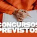 Pessoa segurando agenda aberta e escrevendo, com suéter laranja e texto concursos previstos.