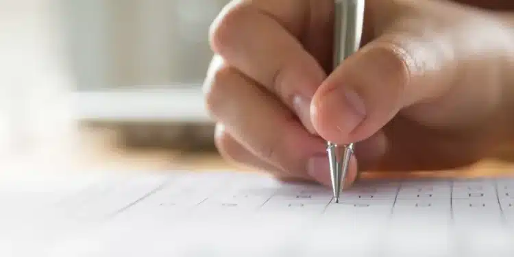 Mão preenchendo gabarito de prova com caneta representando concurso público municipal.