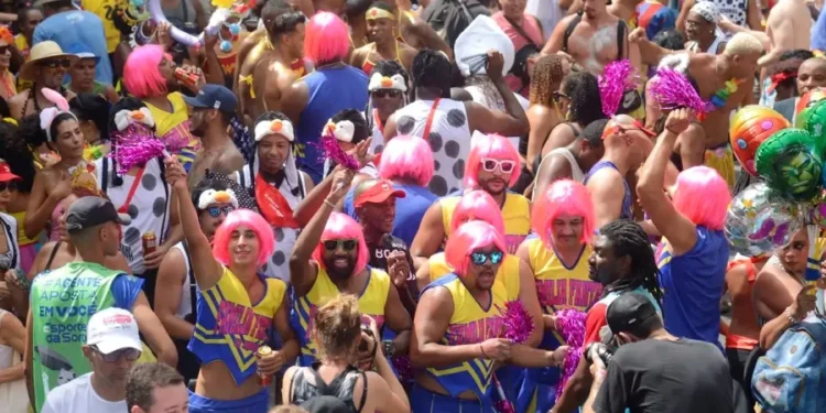 Bloco de Carnaval com foliões usando perucas cor-de-rosa e fantasias, destacando a data e as folgas de quem tem direito ao feriado.