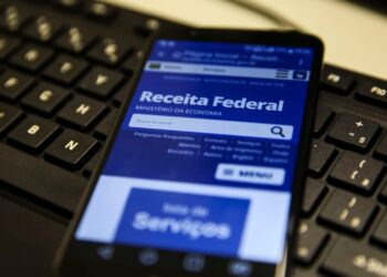 Tela de smartphone exibindo site da Receita Federal, apoiada em teclado.