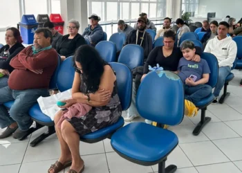 Pessoas aguardando em uma sala de espera para o mutirão do INSS, com bancos azuis e lixeiras ao fundo, em diversos estados do Brasil.