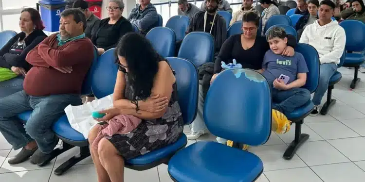 Pessoas aguardando em uma sala de espera para o mutirão do INSS, com bancos azuis e lixeiras ao fundo, em diversos estados do Brasil.