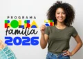 Cartão do Bolsa Família 2026 sendo mostrado por uma mulher sorridente, com dinheiro em notas brasileiras visíveis ao fundo.