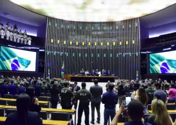 Sessão na Câmara dos Deputados com policial em destaque, em ambiente formal e institucional.
