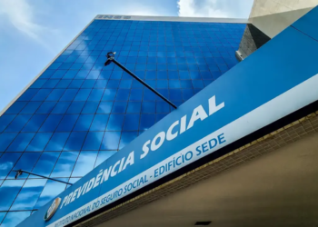 Fachada do edifício sede do INSS com letreiro Previdência Social e estrutura de vidro espelhado azul.