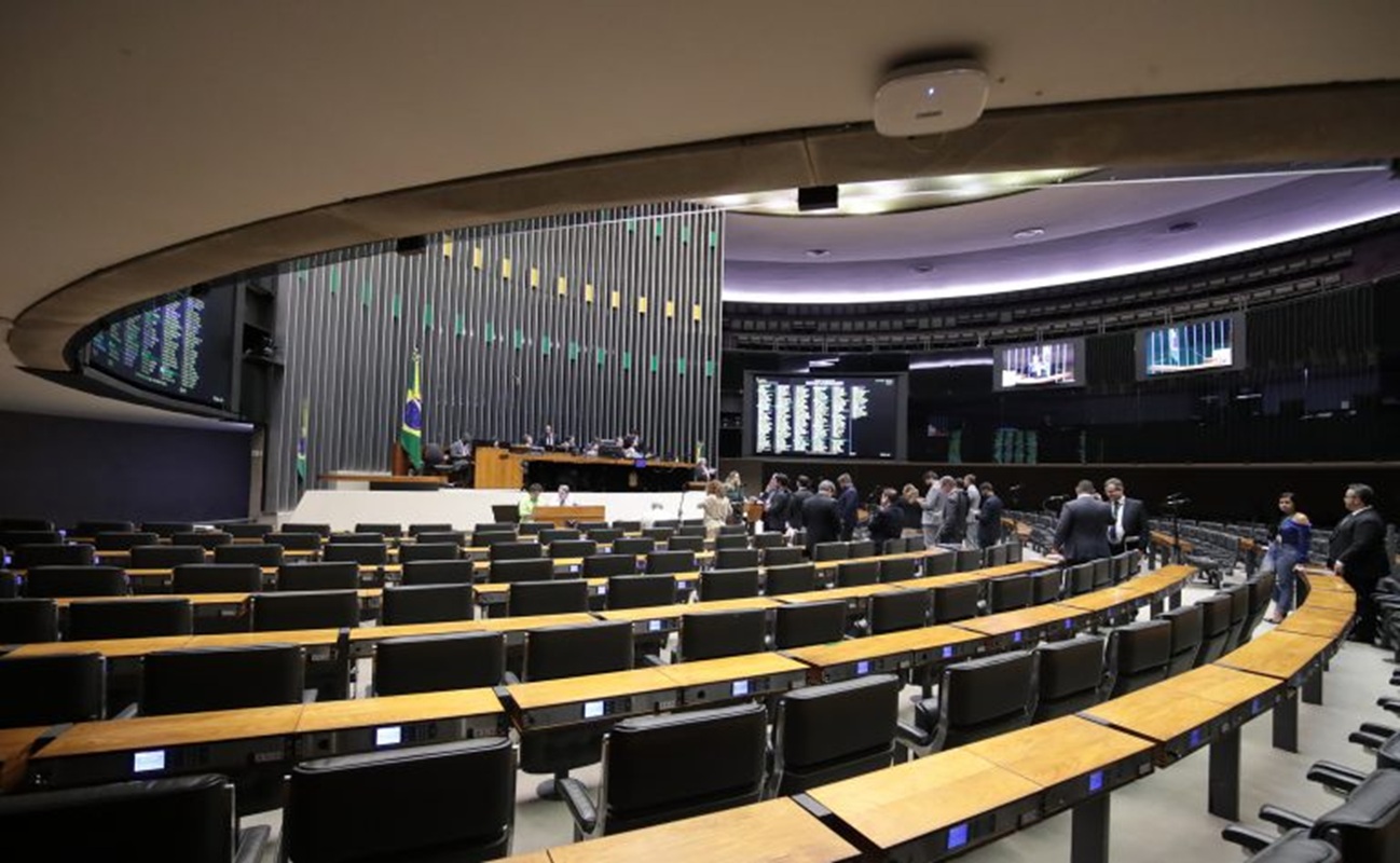Concurso exige nível superior e outros requisitos específicos para atuar na Câmara Vista interna do plenário da Câmara dos Deputados com cadeiras dispostas em semicírculo e bandeira do Brasil ao fundo