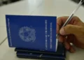 Carteira de Trabalho e Previdência Social sendo preenchida com caneta, representando o processo de solicitação do Seguro-Desemprego.