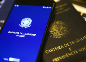 Celular com aplicativo Carteira de Trabalho Digital sobre documento físico da CTPS