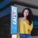 Mulher sorrindo ao lado de placa da Caixa Econômica Federal anunciando liberação de benefício para novos brasileiros