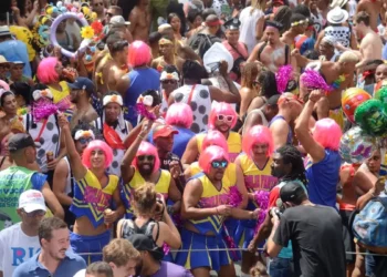 Participantes do Carnaval de 2026 se divertem em um bloco de rua com fantasias coloridas e perucas rosas, celebrando a folia com muito entusiasmo, representando o Carnaval em 2026.