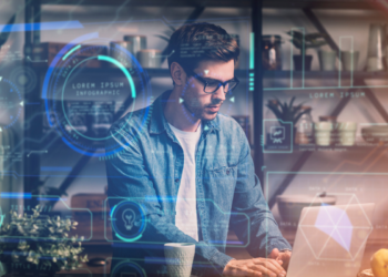 Homem jovem com óculos e camisa jeans usando laptop com gráficos digitais futuristas sobrepostos