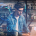 Homem jovem com óculos e camisa jeans usando laptop com gráficos digitais futuristas sobrepostos