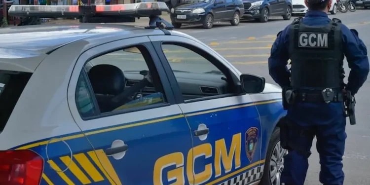 Imagem de um guarda municipal em patrulhamento ao lado de um veículo da Guarda Municipal com a inscrição 'GCM' visível.