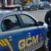 Imagem de um guarda municipal em patrulhamento ao lado de um veículo da Guarda Municipal com a inscrição 'GCM' visível.